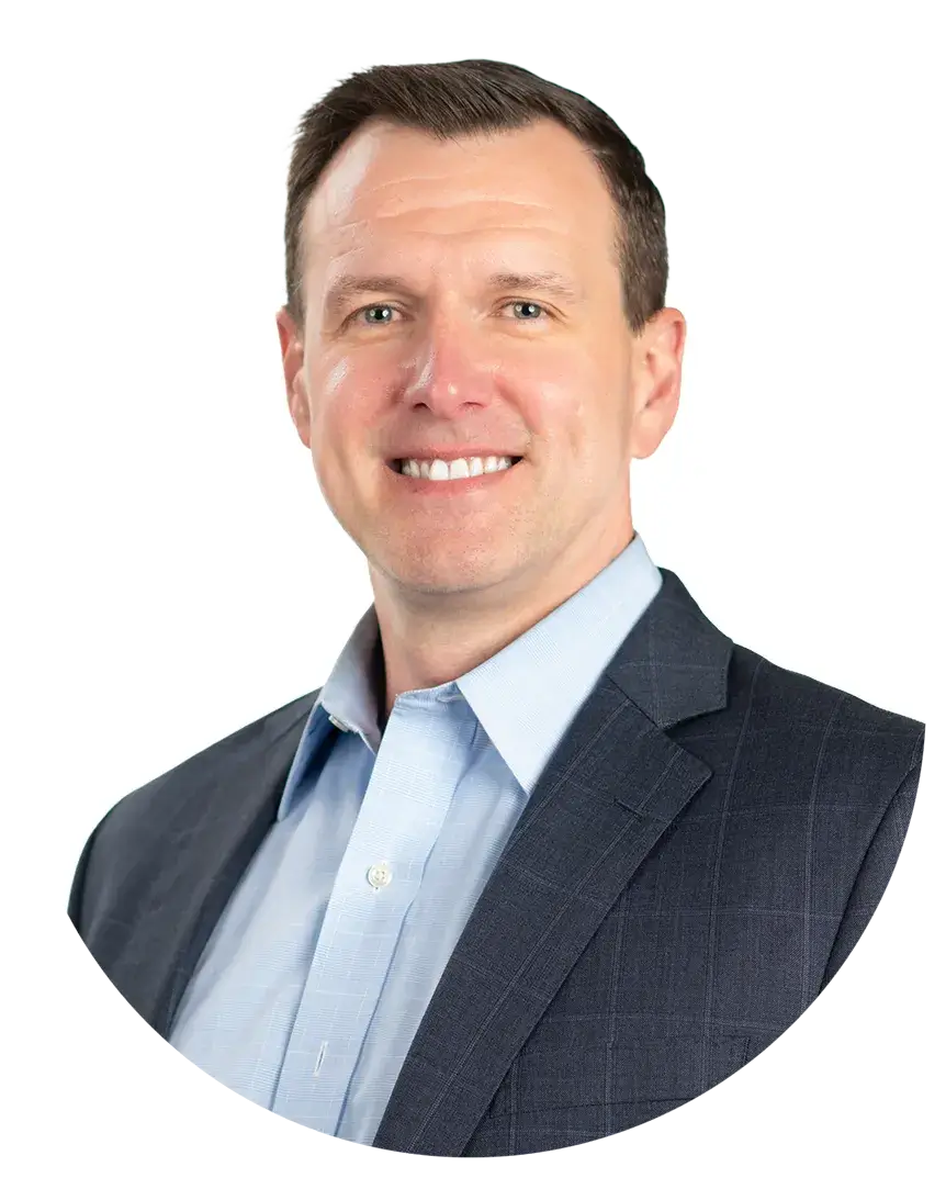 Man in business attire with a light blue shirt and dark blazer, smiling at the camera against a plain white background.