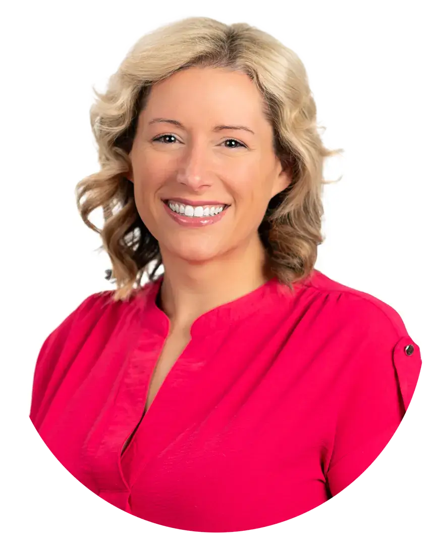 Smiling woman with wavy blonde hair wearing a bright pink blouse, photographed against a plain white background.