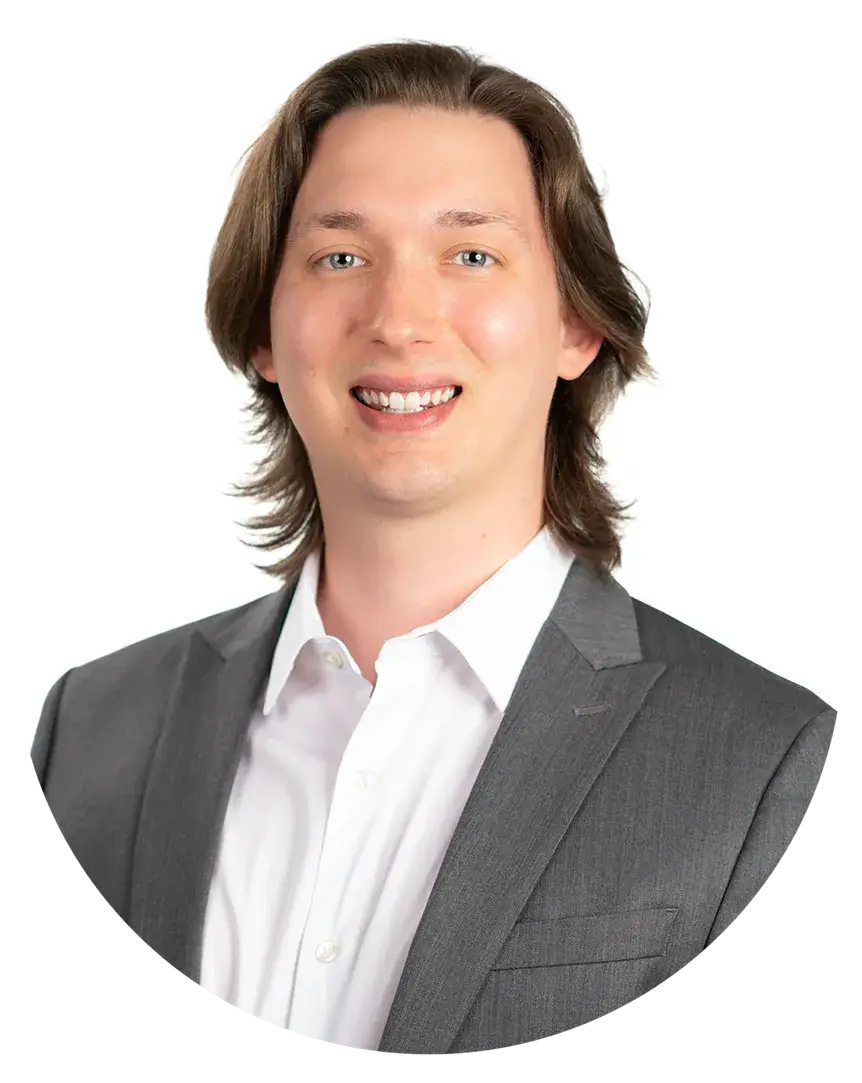 A man with shoulder-length brown hair wearing a gray suit jacket and white shirt, smiling at the camera against a white background.