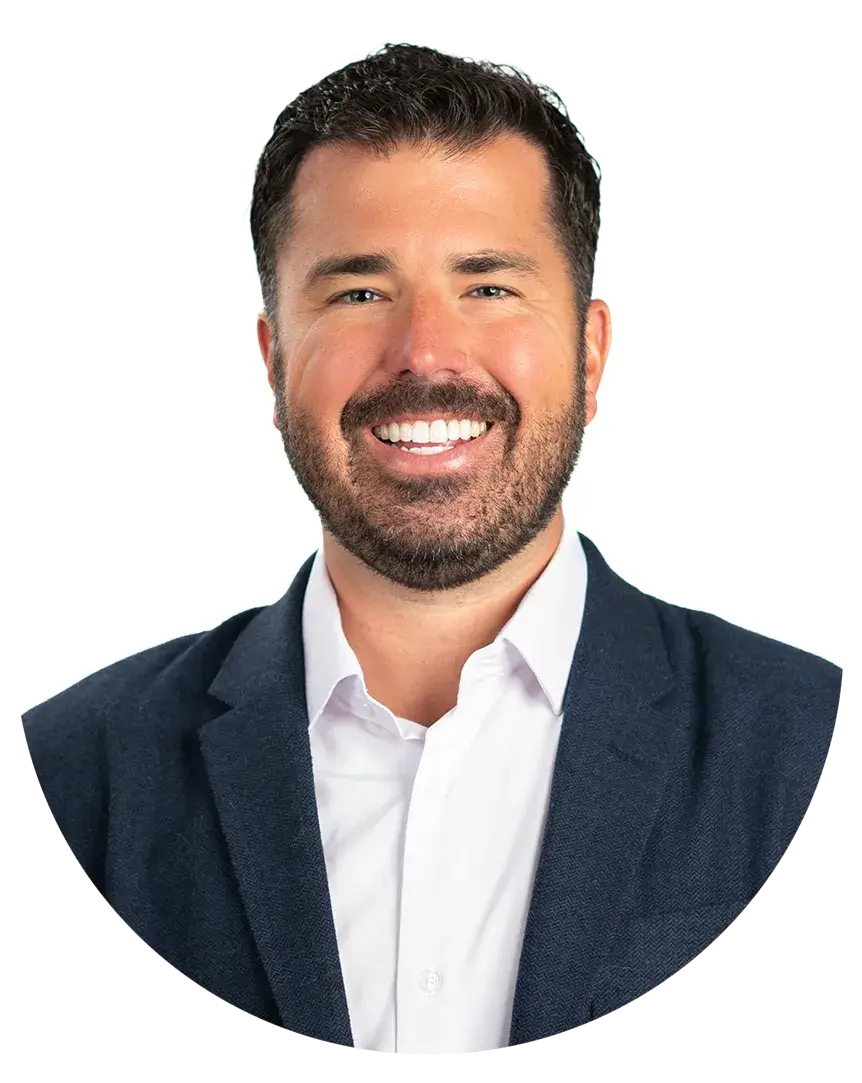 Smiling man with short dark hair and beard wearing a white shirt and navy blazer against a plain white background.
